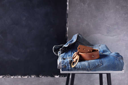 Denim jeans jacket suit and belt at shelf near grey wall background texture. Stack of classic jeans fashion at tableの写真素材