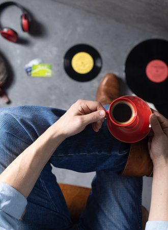 Men's hand holding cup of coffee and leg in jeans with old travel leather boots shoes. Relax and art music life style conceptの写真素材