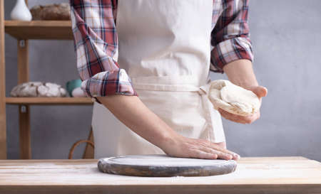 Baker man kneading or making dough and bakery ingredients for homemade bread cooking on shelf. Bakery concept near wall background textureの写真素材