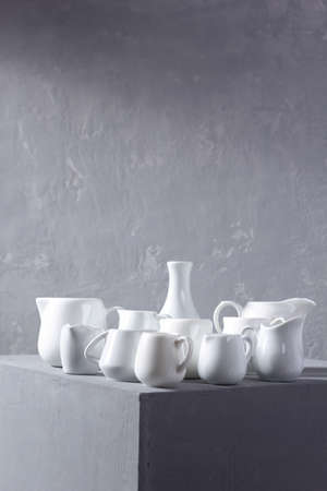 Empty milk jars or creamers dishes set. Kitchen dishware and tableware on grey cube near wall background textureの写真素材