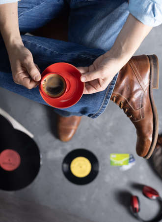 Men's hand holding cup of coffee and leg in jeans with old travel leather boots shoes. Male fashion and art music life style conceptの写真素材