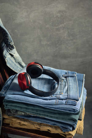 Denim jeans and headphones at old wooden chair near grey wall background texture.  Stack of classic jeans fashion at abstract surfaceの写真素材