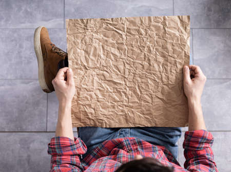 Men's hand holding wrinkled old craft paper blank. Male hand and crumpled paper, top viewの写真素材