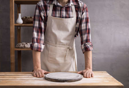 Baker man and pizza board for homemade bread cooking at table. Bakery concept and wooden table background textureの写真素材