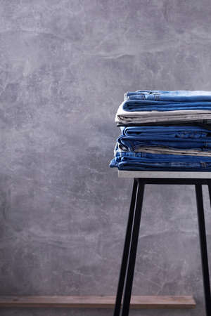 Denim jeans at old stool or shelf near wall background texture. Modern casual style and stack of jeansの写真素材