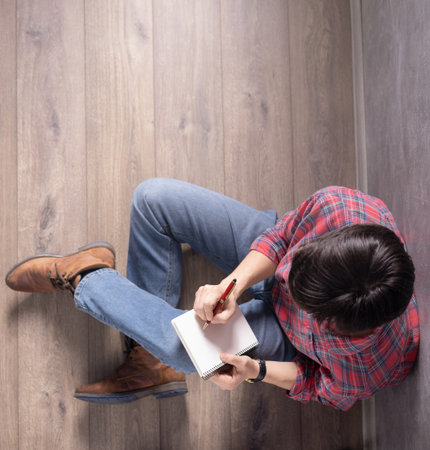 Man sitting on floor thinking with notebook and pen.の写真素材