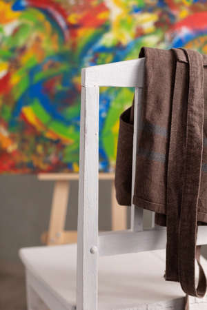 Oil painting and wooden chair with apron. Art still life and paintbrush painting in artist creative studio interior with painter toolの写真素材