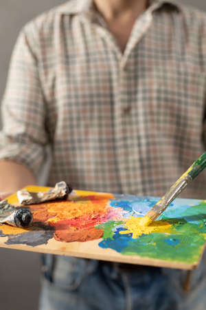 Man painter holding paint palette with paint brush. Young artist and paintbrush painting in creative studioの写真素材