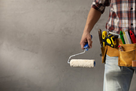 Construction worker man holding paint roller tool near concrete or plaster wall. Male hand and construction tools for house room renovation. Home renovation conceptの写真素材