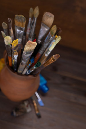 Paint brush in clay jug and used tubes on wooden table background texture. Paintbrush for painting as artistic paint still life. Abstract art conceptの写真素材