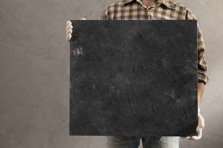 Man worker holding tile near wall. Male hand and plaster background texture. Renovation or repair conceptの写真素材