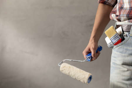 Construction worker man holding paint roller tool near concrete or plaster wall. Male hand and...