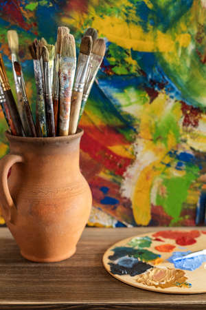 Paint brush in clay jug and art painting abstract background texture. Paintbrush for oil painting as artistic paint still life. Abstract art conceptの写真素材