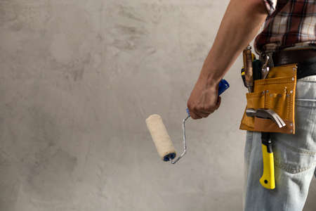 Construction worker man holding paint roller tool near wall. Male hand and construction tools for house room renovation. Home renovation conceptの写真素材