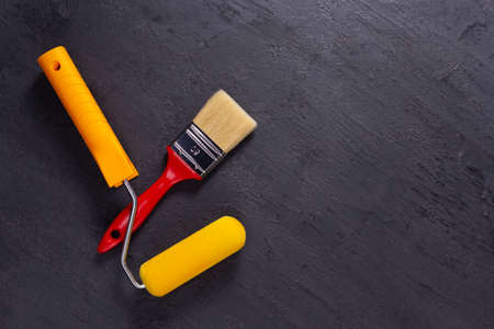 Paintbrush tool and paint roller at black background. Construction tools for house room renovationの写真素材