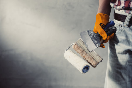 Construction worker man holding tool near concrete or plaster wall. Male hand and construction tools for house room renovation. Home renovation conceptの写真素材