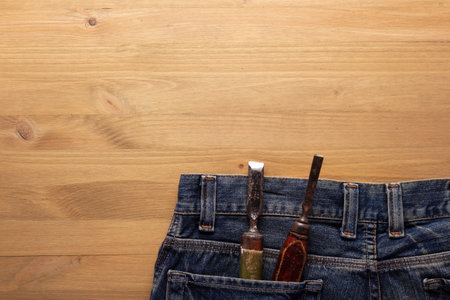 Chisel woodwork tools in jeans pocket at wooden table background. Woodworking conceptの写真素材