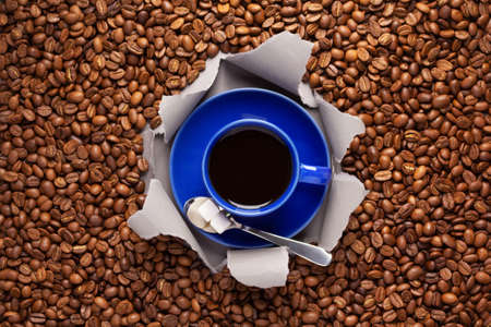 Cup of coffee and beans in torn paper. Coffee ingredients with espresso at tableの写真素材