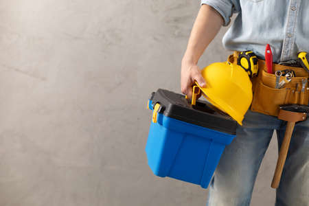 Worker man holding construction helmet tool and toolbox near concrete or cement wall. Male hand and hard hat for house room renovation. Home renovation conceptの写真素材