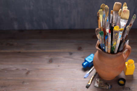 Paint brush in clay jug and tools on wooden table background texture. Paintbrush for painting as artistic paint still life. Abstract art conceptの写真素材