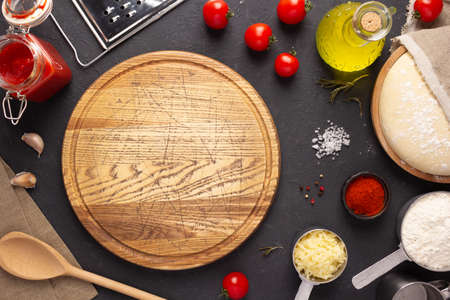 Pizza cutting board with ingredients at table. Dough for pizza on tabletop background. Recipe concept in kitchenの写真素材