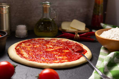 Pizza and dough homemade cooking with ingredients at table. Pizza with sauce on tabletop background. Recipe concept in kitchenの写真素材