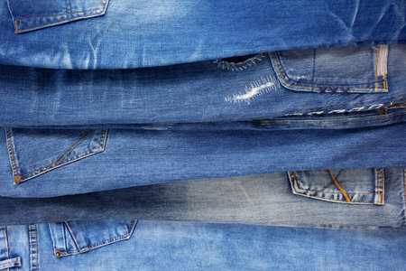 Blue jeans denim heap background. Jeans fabric stack and pocket as material surfaceの写真素材