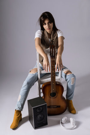 Young woman holdilng acoustic guitar sitting on a chair. Musician in studio with classic guitarの写真素材