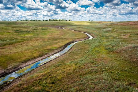South of Russia, spring in the Kalmyk steppes. Brook, drying up by the hot Kalmyk summer, crossing the ravines, against the background of an invasive sky.の写真素材