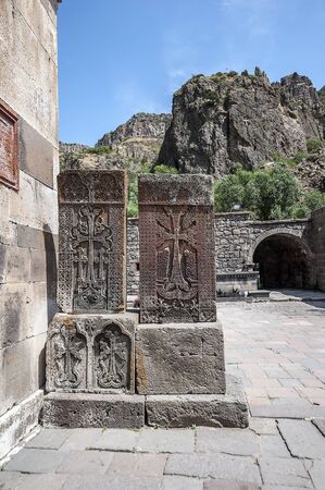 Armenia, ancient khachkars in the courtyard of Geghard monastery against the background of a cliff with an incised gold-plated cross.の写真素材