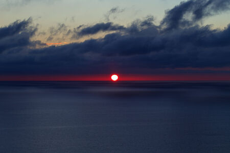 red sun at dark blue sea with blue clouds