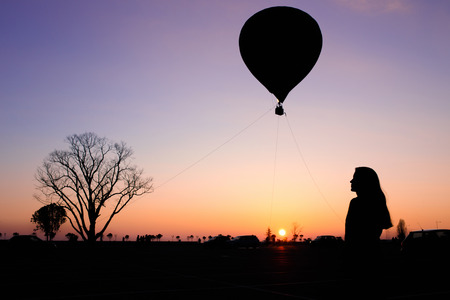 Silhouette of the girl, tree and balloon on a colorful sunsetの写真素材