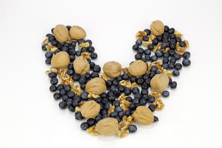 Whole fruit berry and unshelled and shelled nuts outline a shape of love on reflective white.の写真素材