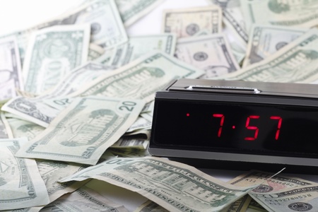 Older digital clock with a drowse button ticking time with United States paper dollars of various amounts all around randomly.の写真素材