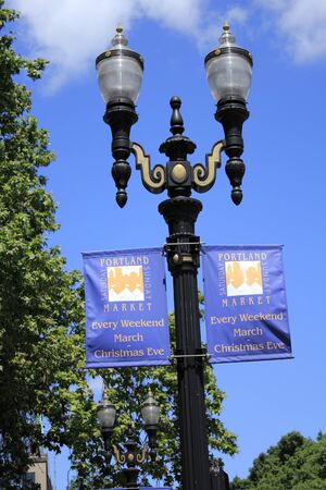 PORTLAND, OREGON - JULY 28, 2012: Two Portland Saturday Sunday Market signs hung below street lights with trees and a beautiful sunny blue sky in the background in Portland, Oregon.のeditorial素材
