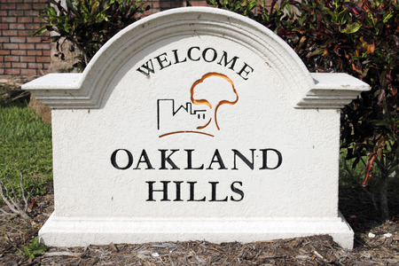 OAKLAND PARK, FLORIDA - JULY 1, 2013   Painted cement Oakland Hills Welcome sign with graphic seen closeup outside on a sunny day with tropical foliage and a brick wall behind it のeditorial素材
