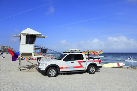 POMPANO BEACH, FLORIDA - DECEMBER 22, 2013  Pompano Beach Ocean Rescue truck next to a lifeguard tower with rescue surfboards, safety warning flags, with people and the Atlantic ocean on a sunny day のeditorial素材