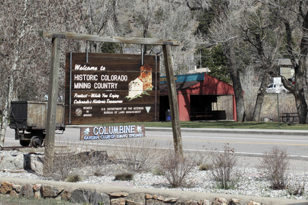 Idaho Springs, CO, USA - April 21, 2014: Old wooden sign welcoming visitors to historic Colorado mining country with other information. The sign has a painting of the towns Argo Mine as well as a genuine mining cart behind the sign on a sunny spring day.のeditorial素材