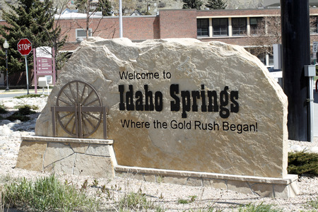 Idaho Springs, CO, USA - April 23, 2014: Large tan stone that has written on and carved into it, Welcome to Idaho Springs, Where the Gold Rush  Began! The sign also has a brown sculpture of a water wheel on a sunny day in this small town.のeditorial素材