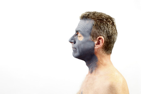 Adult male in his forties facing left wearing a dark gray charcoal and bentonite mud mask. A guy with a charcoal and bentonite mud mask skin treatment on his faceの写真素材