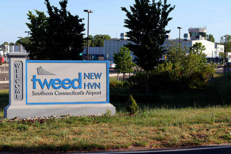 New Haven, CT, USA - May 27, 2021: Entrance sign to Tweed New Haven airport code, HVN, on a sunny evening with airport in back. Tweed New Haven airport entry sign with airport and a plane in background.のeditorial素材