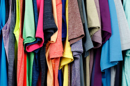 Close-up of a many different menâs sleeveless shirts, t-shirts and polo shirts seen from a side view. Sideview of menâs polo shirts, teeshirts and sleeveless shirts hanging in a closet close-up.の写真素材