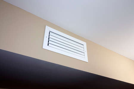 A white rectangle heating and cooling outflow air vent from a duct of an indoor HVAC system in a...