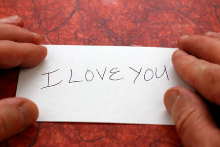 I love you printed in black on a white piece of paper with white male fingers on each side of the...