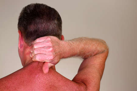 Mature adult white male seen from rear view massaging the back of his neck under his brown hair. Rear view of a naked caucasian man massaging his painful neck to help to relax his muscles close-upの写真素材