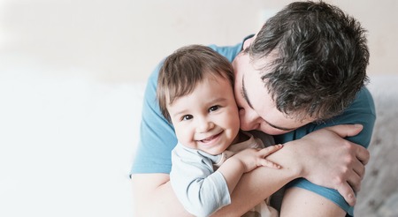 Close-up portrait of happy young father hugging and kissing his sweet adorable child. Indoors shot,...