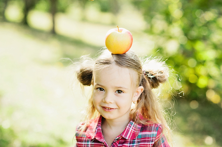 Girl with Apple in the Apple Orchard. Beautiful Girl with Organic Apple in the Orchard. Harvest Concept. Garden, Toddler eating fruits at fall harvest.の写真素材