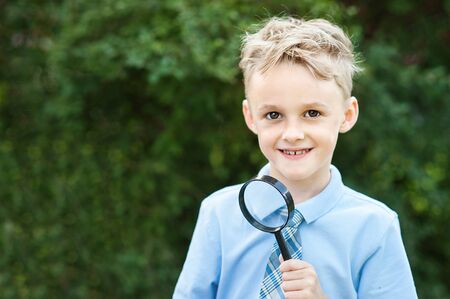 Portrait of a Schoolboy looking through a magnifying glass on the background autumn park. Farewell Bell. day of knowledge. beginning of the school year.の写真素材