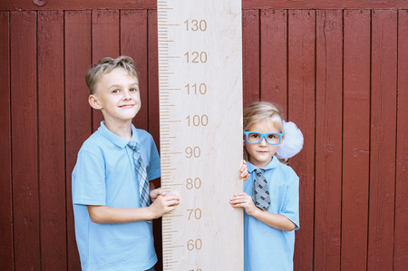 girl and schoolboy with big ruler standing on wood backgroundの写真素材
