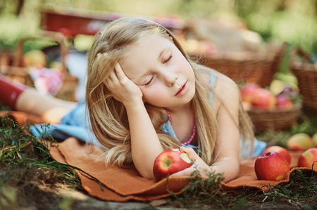 Girl with Apple in the Apple Orchard. Beautiful Girl Eating Organic Apple in the Orchard. Harvest Concept. Garden, Toddler eating fruits at fall harvest. Apple picking.の写真素材
